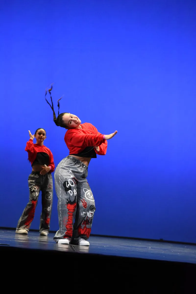 Due ballerine in abiti rossi e pantaloni decorati si esibiscono su un palco blu.