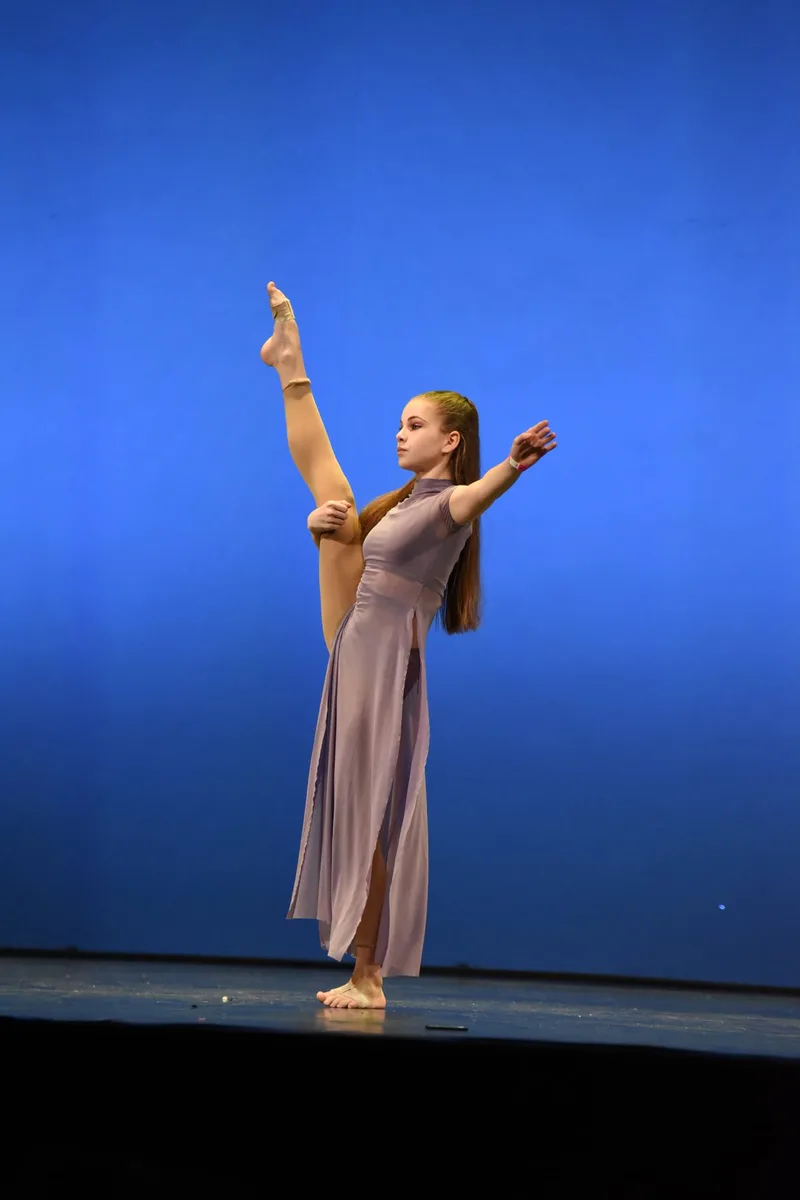 Una ballerina in abito beige esegue un’estensione della gamba sul palco.