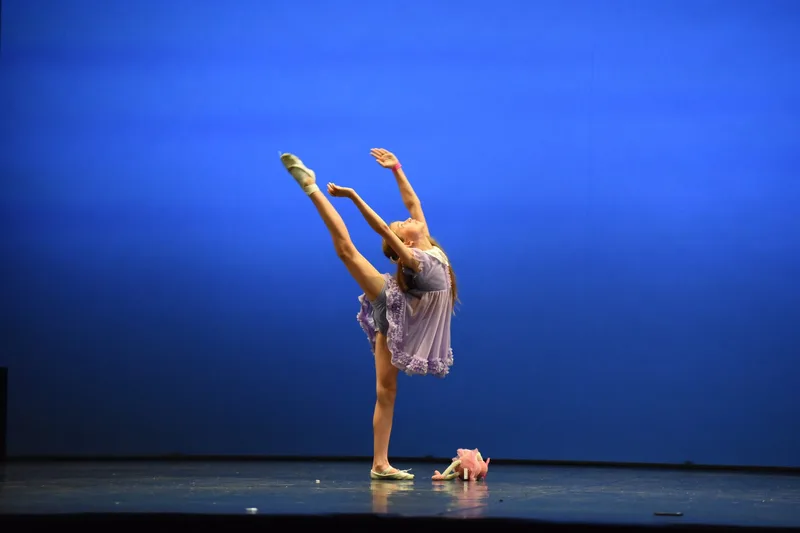 Una ballerina in costume chiaro mantiene un’estensione verticale della gamba.