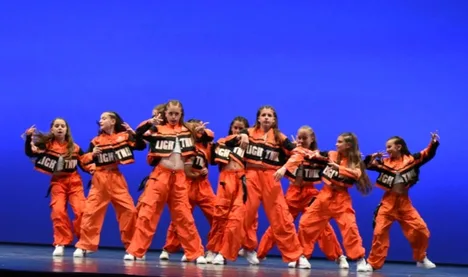 Un gruppo di giovani ballerine in pantaloni arancioni esegue una coreografia hip-hop.
