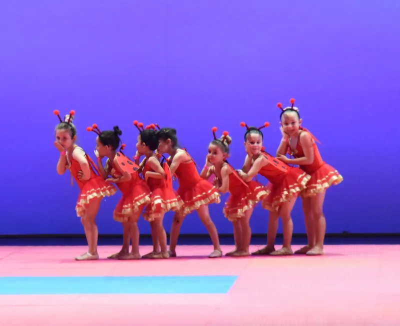 Un gruppo di bambine in costumi rossi con paillettes danza in formazione.