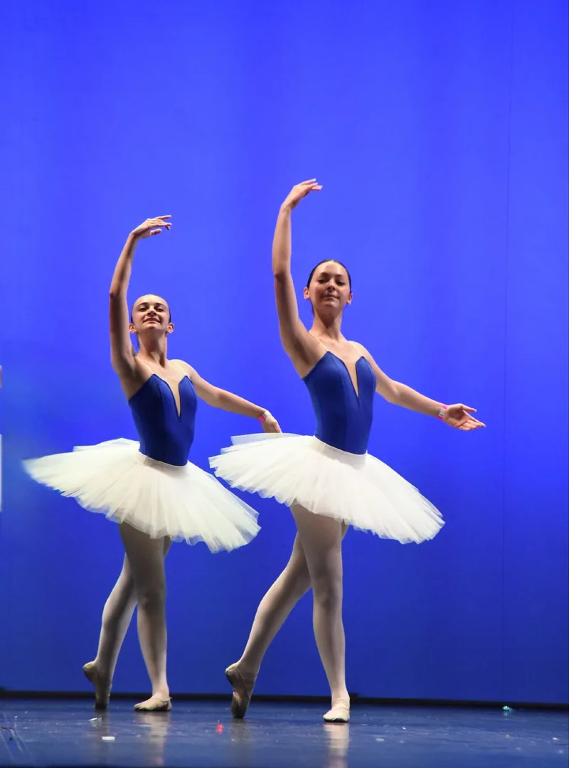 Due ballerine in tutù bianchi e body blu posano insieme sul palco.