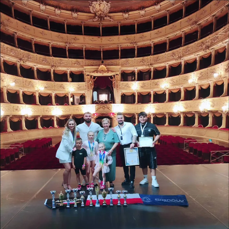 Un gruppo posa sul palco di un teatro dietro una fila di trofei.