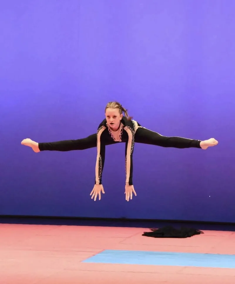 Una ginnasta in costume nero è sospesa in un salto sopra la pedana.