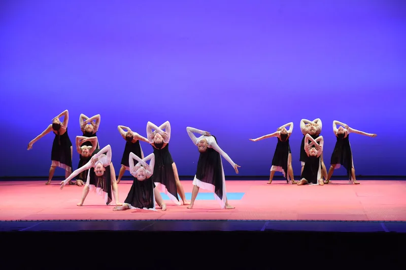 Un gruppo in costumi bianchi e neri forma figure geometriche sulla pedana.