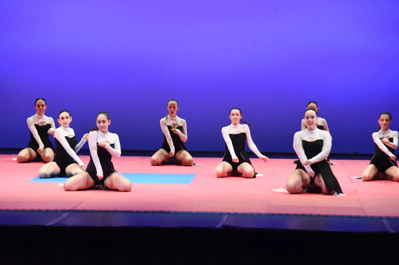 Un gruppo di ballerine in costumi bianchi e neri posa in ginocchio sul palco.